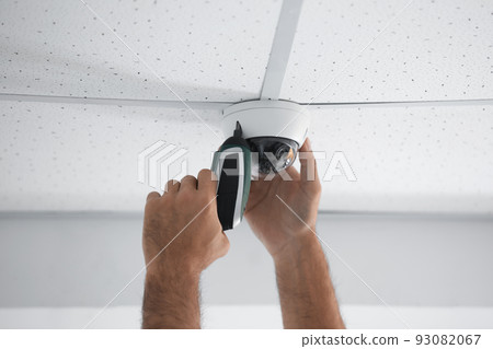 Technician installing CCTV camera on ceiling indoors, closeup 93082067