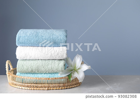 Wicker tray with folded bath towels and beautiful flower on grey table. Space for text 93082308