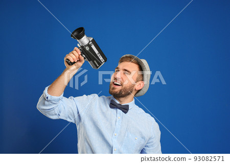 Young man with vintage video camera on blue background 93082571