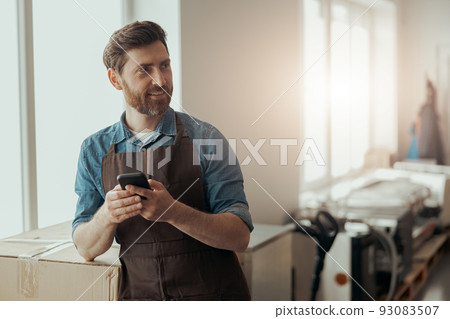 Man worker of small coffee roasting factory holding phone on his workplace Man worker of small coffee roasting factory holding phone on his workplace 93083507