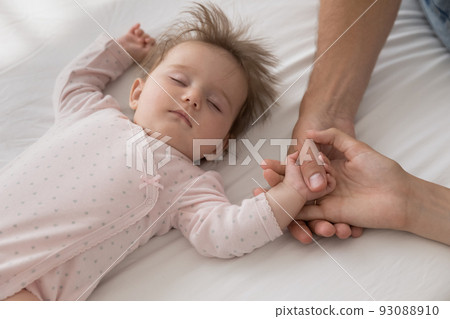 Cute newborn sleeping on bed touch loving parents hands 93088910