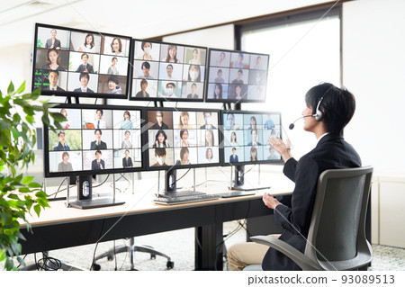 A man having a video conference with a large number of people while looking at multiple monitors 93089513