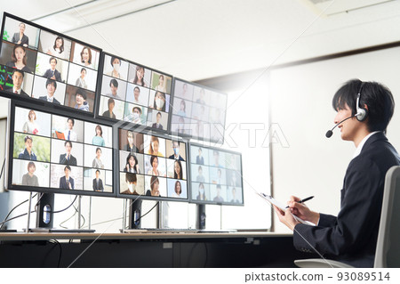 A man having a video conference with a large number of people while looking at multiple monitors 93089514