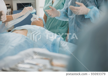 Close up hands of doctor anesthesiologist holding breathing mask on patient face during operation Close up hands of doctor anesthesiologist holding breathing mask on patient face during operation 93093379