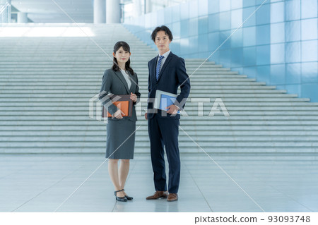 Young businessman and businesswoman standing in office lobby Young businessman and businesswoman standing in office lobby 93093748