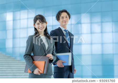 Young businessman and businesswoman standing in office lobby Young businessman and businesswoman standing in office lobby 93093760