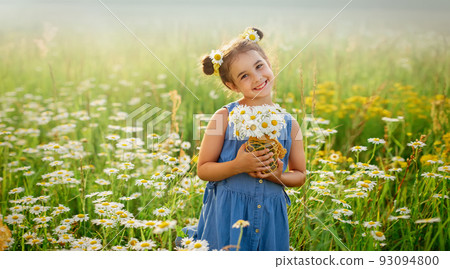 Pretty smiling little girl with a bouquet of daisies , stands in a field with daisies 93094800