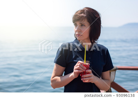 Pretty woman drinking fruit smoothie through a straw against the background of the sea Pretty woman drinking fruit smoothie through a straw against the background of the sea 93096138