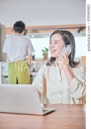 A woman who makes a phone call on a smartphone in telework and a man who does housework A woman who makes a phone call on a smartphone in telework and a man who does housework 93098965