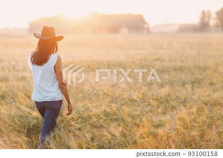 Woman farmer in cowboy hat at agricultural field on sunset. Woman farmer in cowboy hat at agricultural field on sunset. 93100158