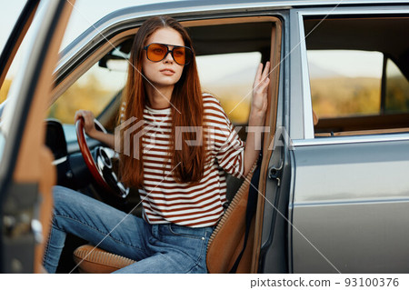 A woman driver in sunglasses stopped the car on the road in a pktkshestvie and is resting looking at a beautiful view 93100376