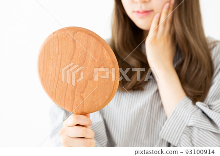 A young woman looking at a hand mirror and doing skin care A young woman looking at a hand mirror and doing skin care 93100914
