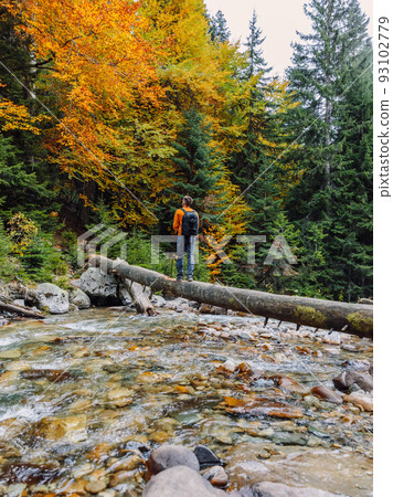 Traveller men on a log over the river in autumnal forest. 93102779