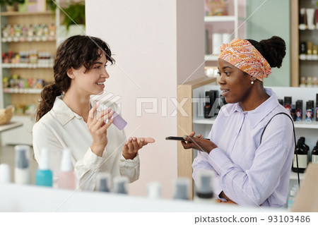Young smiling shop assistant recommending black woman cosmetic product Young smiling shop assistant recommending black woman cosmetic product 93103486