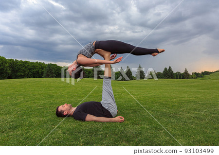 Young couple doing acro yoga in park. Man lying on grass and balancing woman in his feet 93103499