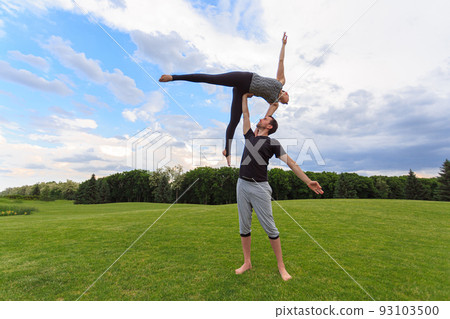 Young healthy couple doing acro yoga in the sunny summer park. Fitness and healthy lifestyle 93103500