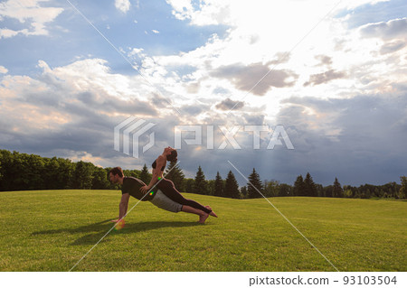 Healthy man lying on grass and balancing woman. Couple doing acrobatic yoga exercise in park Healthy man lying on grass and balancing woman. Couple doing acrobatic yoga exercise in park 93103504