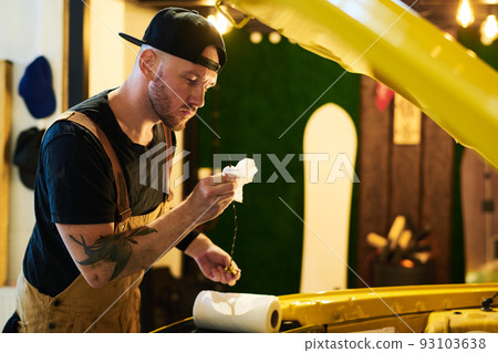 Young man in workwear standing in front of open hood of electric car Young man in workwear standing in front of open hood of electric car 93103638