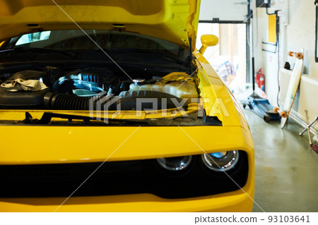 Part of yellow car with open lid of hood standing in garage or workshop Part of yellow car with open lid of hood standing in garage or workshop 93103641