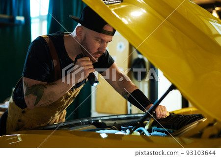 Young mechanic of car repair workshop checking engine of yellow automobile Young mechanic of car repair workshop checking engine of yellow automobile 93103644