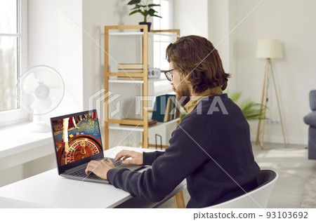 Caucasian man playing in online casino using laptop looking at monitor with roulette wheel 93103692