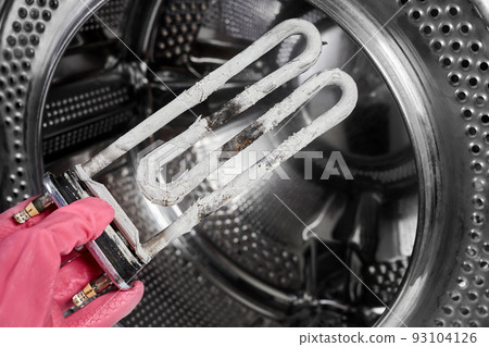 A man holds in his hand a burnt-out heating element of a washing machine against the background of a washing machine drum 93104126
