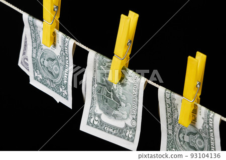 One and two dollar banknotes fastened with clothespins are dried on clotheslines on a dark background One and two dollar banknotes fastened with clothespins are dried on clotheslines on a dark background 93104136