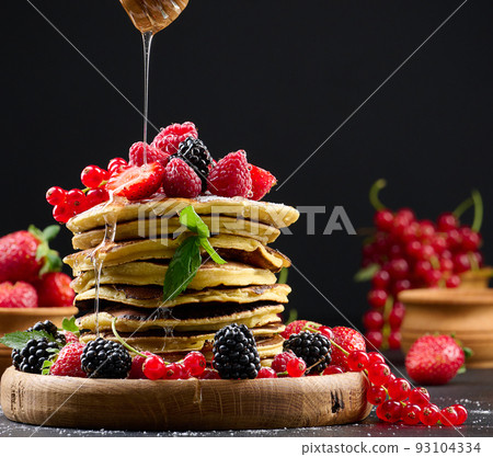 Stack of pancakes with fresh fruit sprinkled with honey on a black background Stack of pancakes with fresh fruit sprinkled with honey on a black background 93104334