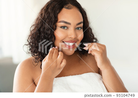 Young black chubby woman cleaning teeth with dental floss at home and looking at camera, performing everyday dental care 93104749