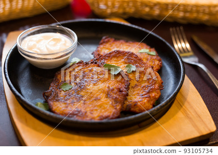 Fried grated potato pancakes with sour cream on frying pan 93105734