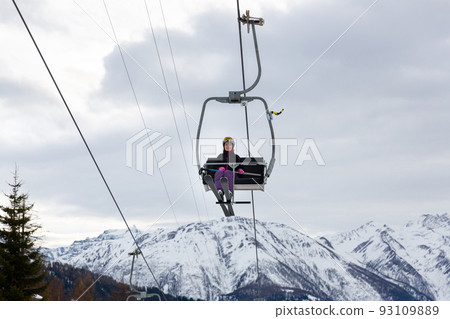 Woman skier riding on chairlift on background of snowy mountains Woman skier riding on chairlift on background of snowy mountains 93109889