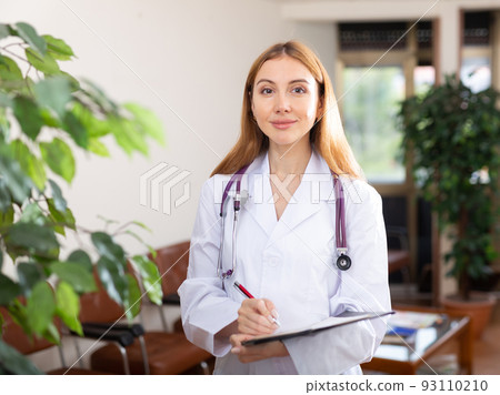 Young woman doctor in white coat filling out medical form at clipboard Young woman doctor in white coat filling out medical form at clipboard 93110210