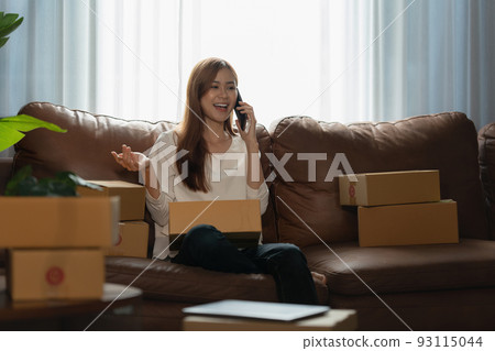 Image of Young asian woman startup freelance with parcel box and talking with customer by phone. Online marketing packing box delivery concept. Image of Young asian woman startup freelance with parcel box and talking with customer by phone. Online marketing packing box delivery concept. 93115044