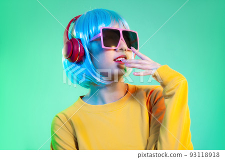 Young asian girl in yellow sweatshirt blue color shot hair style wearing red headphone and pink sunglasses listen to music posing on the green screen background.. Young asian girl in yellow sweatshirt blue color shot hair style wearing red headphone and pink sunglasses listen to music posing on the green screen background.. 93118918
