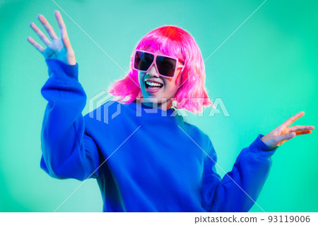 happy asian woman in blue sweatshirt pink short hair punk style wearing sunglasses and headphones dancing on the green background 93119006