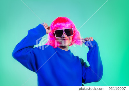 happy asian woman in blue sweatshirt pink short hair punk style wearing sunglasses and headphones dancing on the green background 93119007