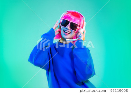 happy asian woman in blue sweatshirt pink short hair punk style wearing sunglasses and headphones dancing on the green background 93119008