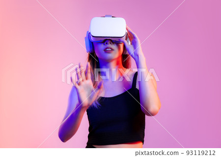 Metaverse concept, young asian woman in black tank top wearing white vr headset watching playing and touching on pink neon color background 93119212
