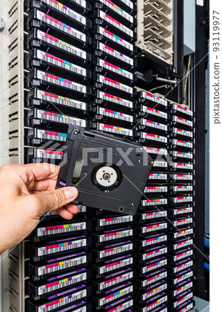hand of a technician holding data storage magnetic tape in front of data storage array hand of a technician holding data storage magnetic tape in front of data storage array 93119977
