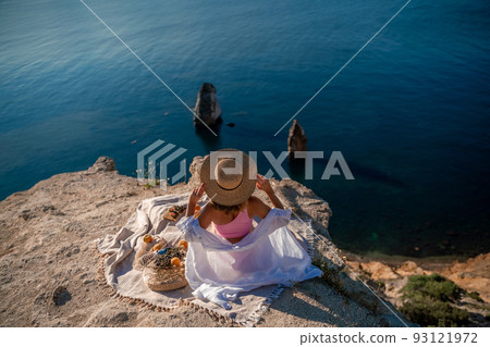 photo of a beautiful woman with long blond hair in a pink shirt and denim shorts and a hat having a picnic on a hill overlooking the sea photo of a beautiful woman with long blond hair in a pink shirt and denim shorts and a hat having a picnic on a hill overlooking the sea 93121972