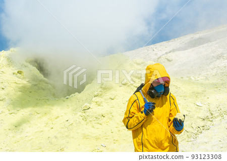 female volcano scientist on the background of a smoking fumarole examines a sample of a sulfur mineral female volcano scientist on the background of a smoking fumarole examines a sample of a sulfur mineral 93123308