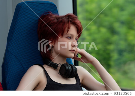 young woman with headphones rides in a moving suburban train and looks out the window 93123565