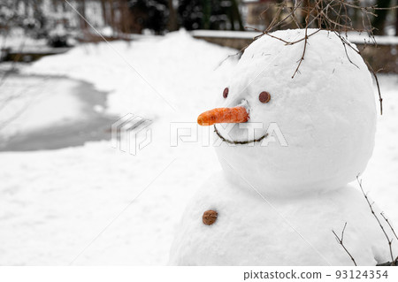Funny snowman with carrot nose, walnut buttons alone near frozen lake in park Funny snowman with carrot nose, walnut buttons alone near frozen lake in park 93124354