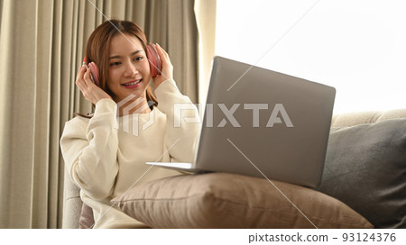 Smiling young woman with headphone using laptop, spending leisure time on a bright autumn morning 93124376