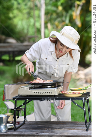 Young woman wearing casual clothing and hat grilled bbq near the river bank surrounded by beautiful nature Young woman wearing casual clothing and hat grilled bbq near the river bank surrounded by beautiful nature 93124381