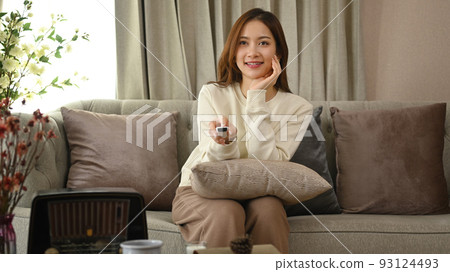 Young woman with remote controller watching TV, spending leisure time in cozy winter or autumn weekend at home 93124493