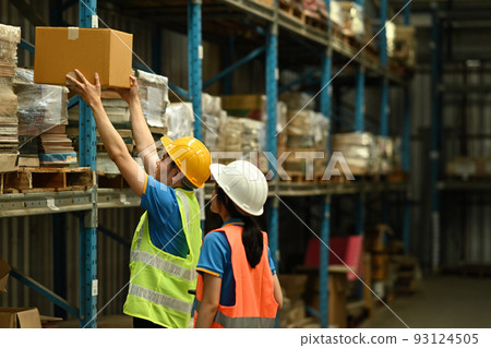 Male warehouse workers and manager wearing hardhats and reflective jackets checking stock in warehouse 93124505