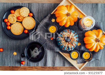 Top view fall composition for Halloween. Orange, gray pumpkins, burning candles on the tray and plate with halloween sweets and hot tea with ghost silhouette inside. Trick or treat. Selective focus. 93125977