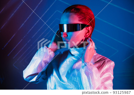 Neon portrait of woman, dressed in futuristic holographic clothes and glasses. Portrait of a cyberpunk girl. Neon blue and pink light. Virtual reality glasses. Fashion, futuristic generation concept. Neon portrait of woman, dressed in futuristic holographic clothes and glasses. Portrait of a cyberpunk girl. Neon blue and pink light. Virtual reality glasses. Fashion, futuristic generation concept. 93125987