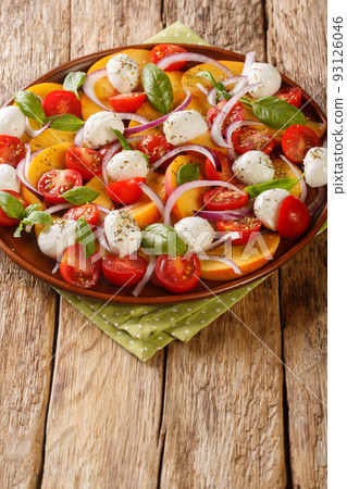 Summer salad with fresh peaches, mozzarella, cherry tomatoes, onion and basil close-up in a plate. Vertical 93126046